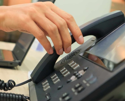 Close-up of someone's hand reaching for an IP phone on a work desk