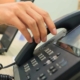 Close-up of someone's hand reaching for an IP phone on a work desk