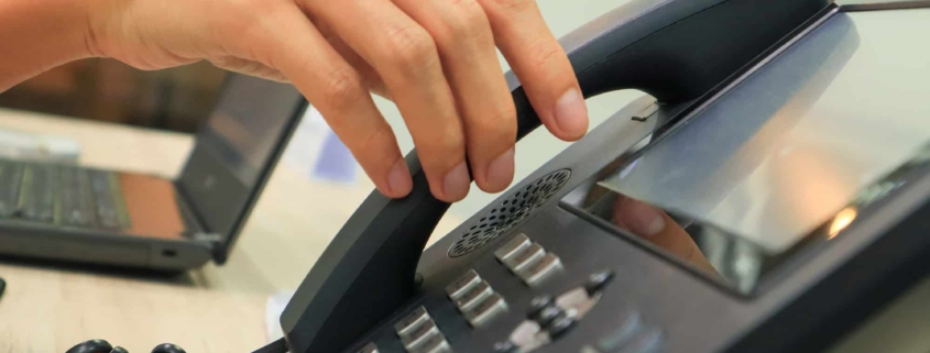 Close-up of someone's hand reaching for an IP phone on a work desk