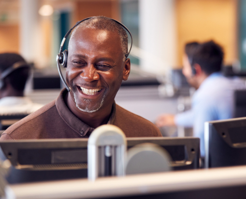 Mature Businessman Wearing Telephone Headset Talking To Caller In Customer Services Department